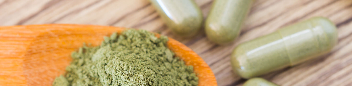 Private label custom green powder formula and capsules being measured with a measuring spoon.